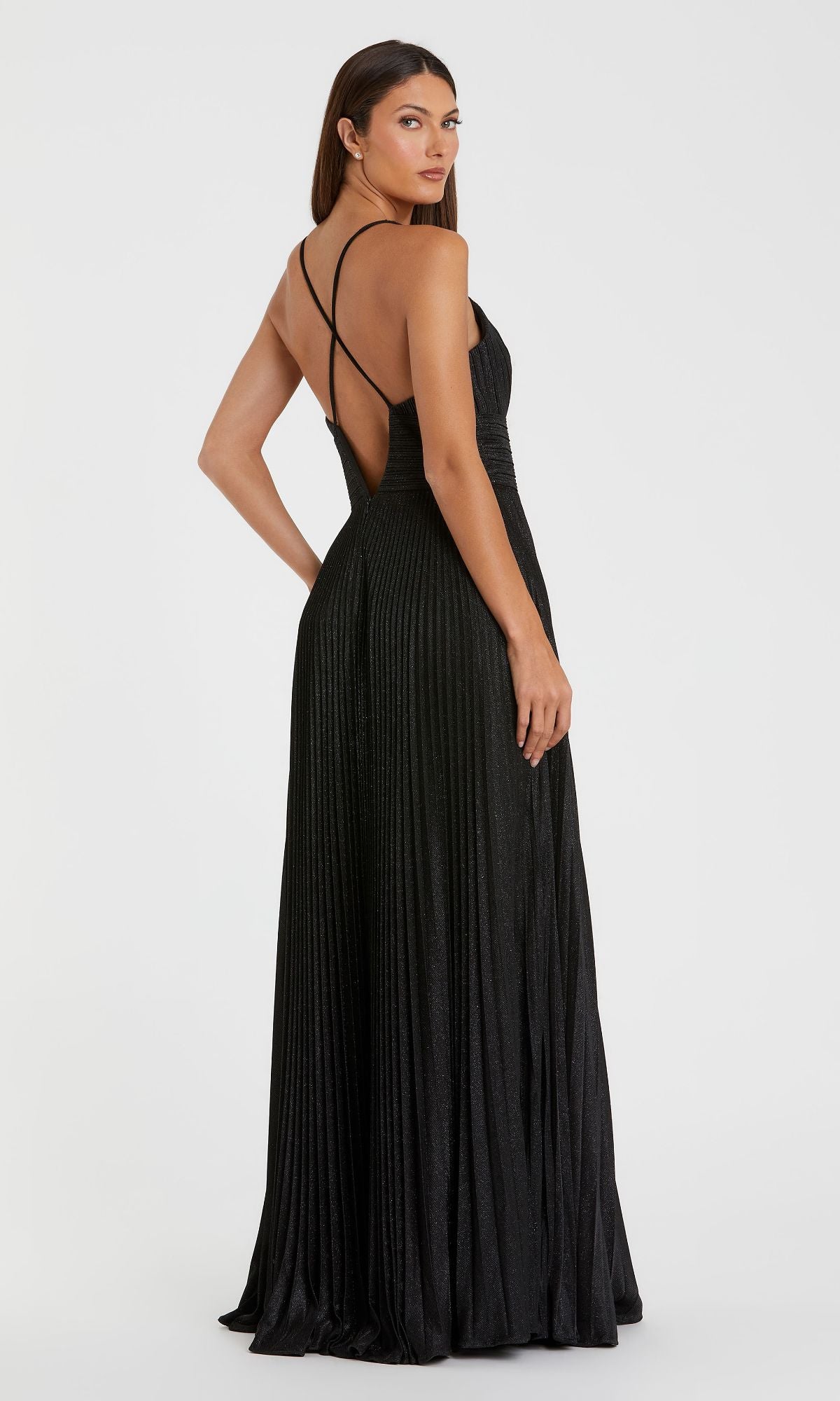 A woman wears the Pleated Empire-Waist Long A-Line Prom Dress 30725, featuring thin crisscross straps, an open back, and black pleated fabric, standing against a plain white background.